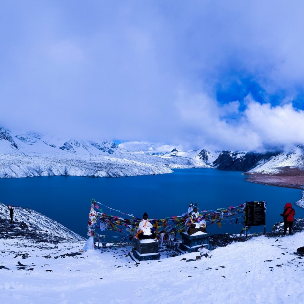 Snow-covered mountains and lake with prayer flags in a scenic Himalayan landscape.