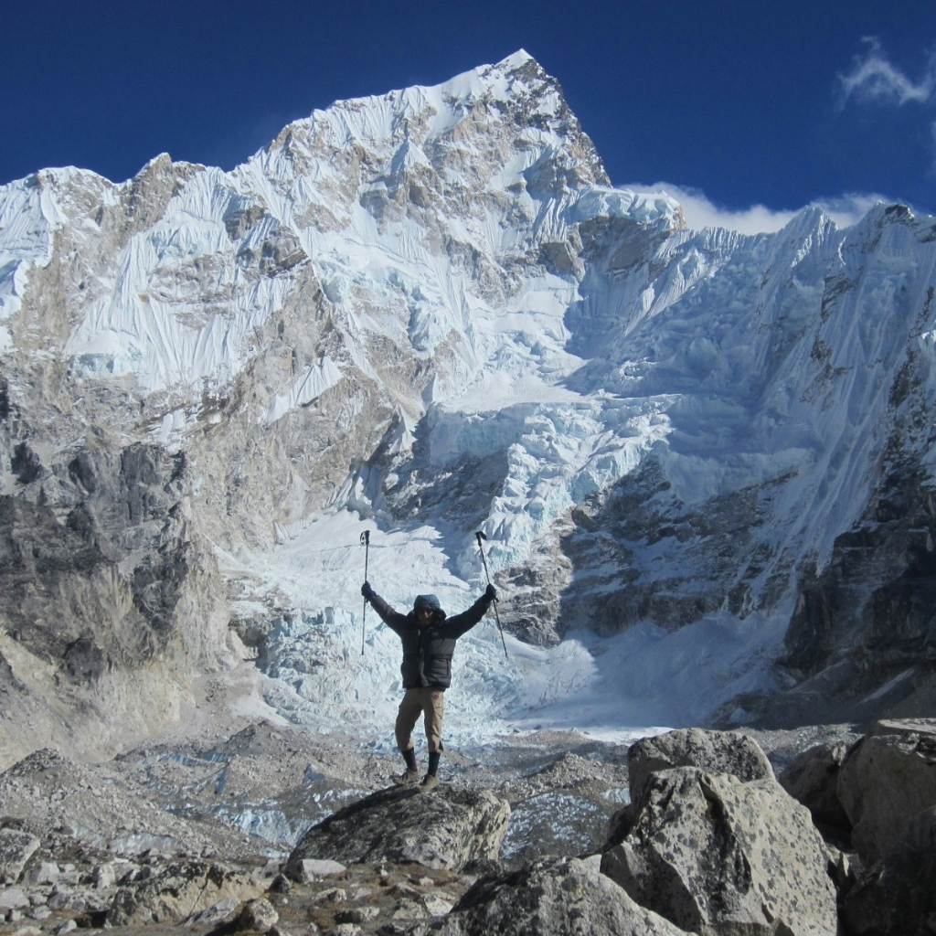 Hiker celebrating on rocky terrain with snow-capped peaks in the background.